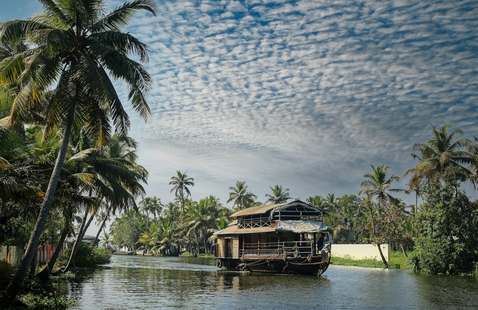 A traditional wooden houseboat moored beside palm trees on the Kerala backwaters